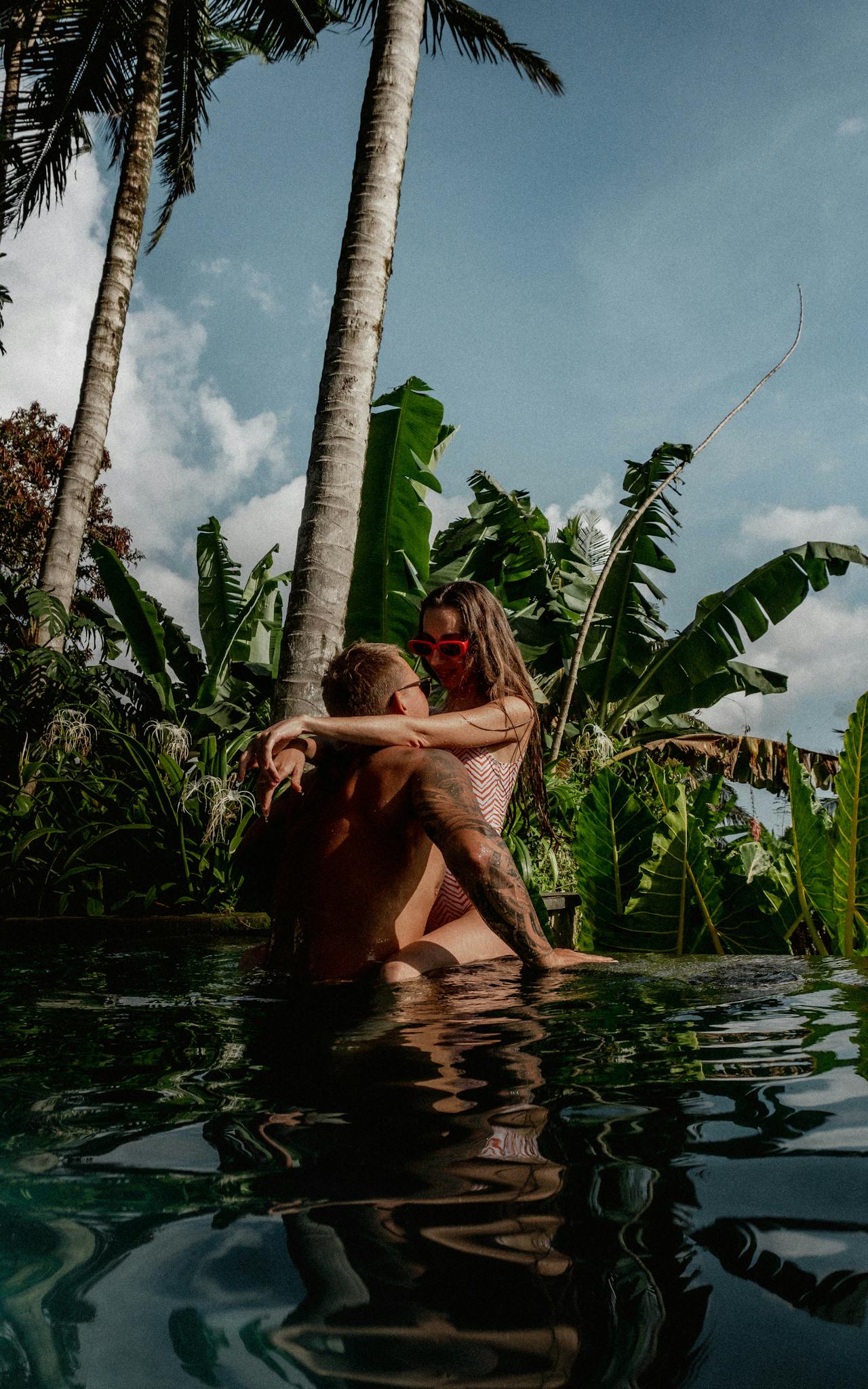 A couple enjoys a warm embrace in a lush tropical swimming pool, surrounded by banana trees.